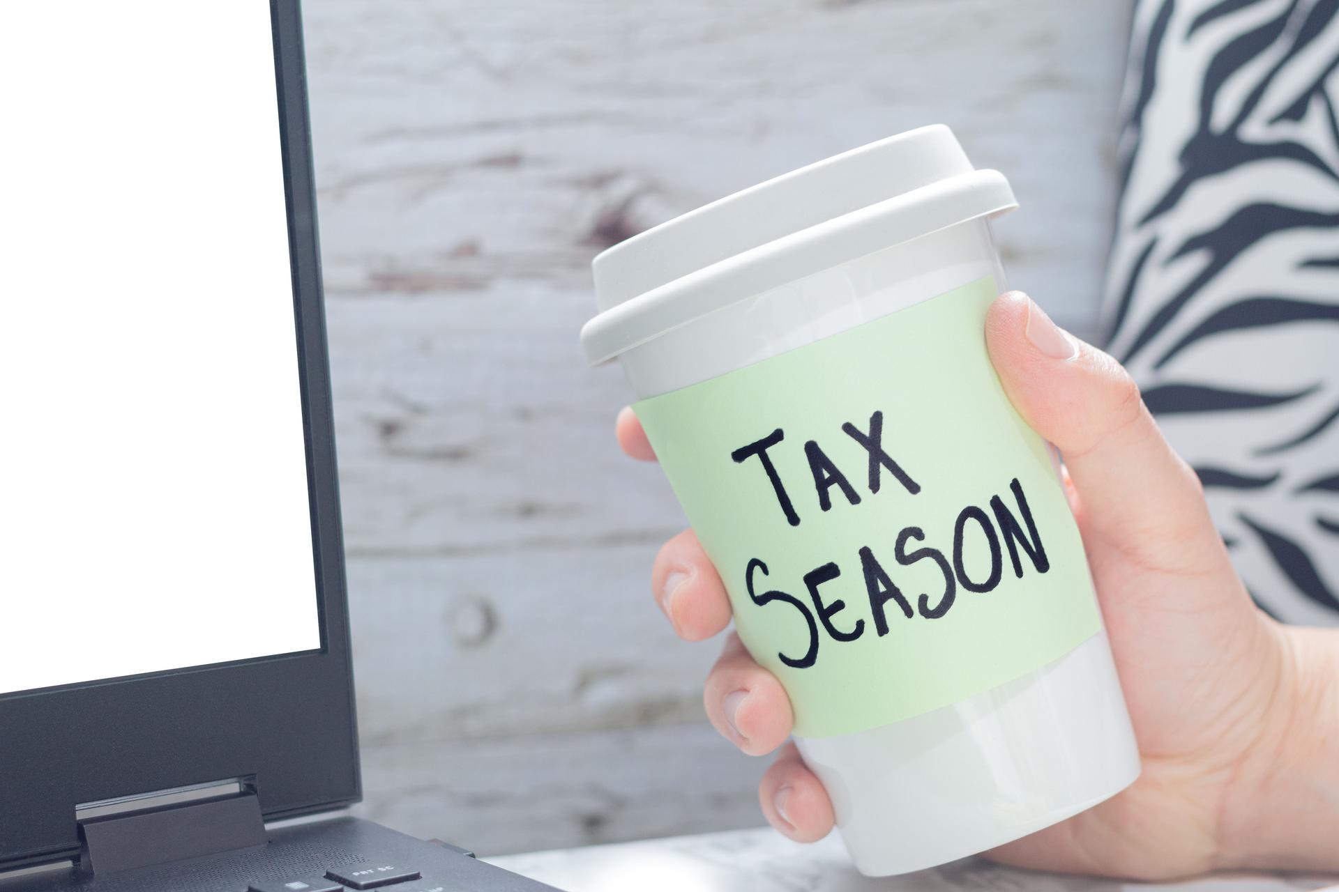 A hand holds a coffee mug with Tax Season message in office environment